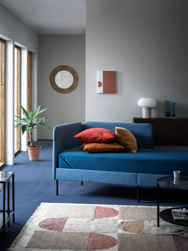 BLÅKULLEN upholstered bedframe in a cool well-lit living room setting placed near a large neutral rug and sleek coffee table.