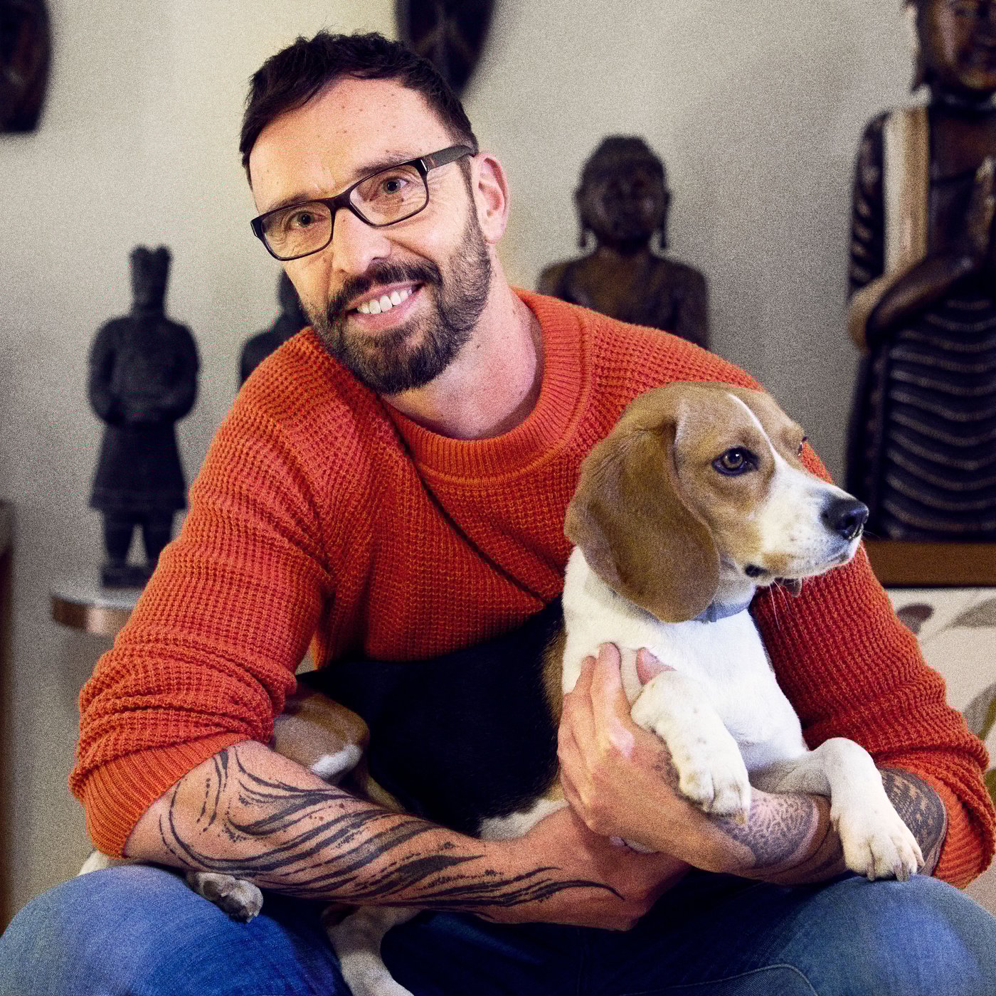 Daniel sitting with his pet Beagle in his living room, a collection of statues in the background.