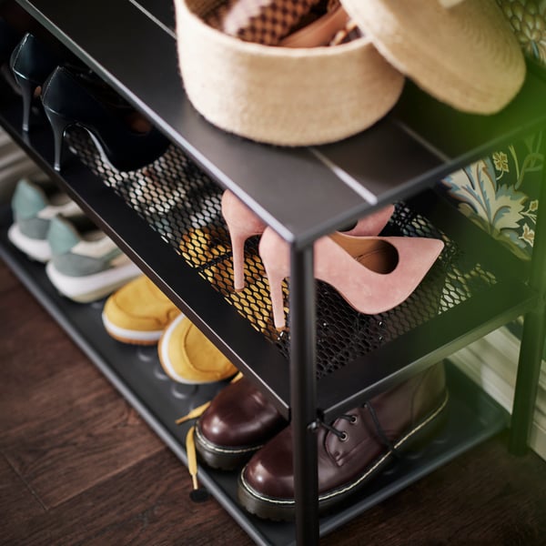 The bench of a black NIPÅSEN coat rack and bench with shoe storage holds various shoes and a LJUNGAN basket with the lid off.