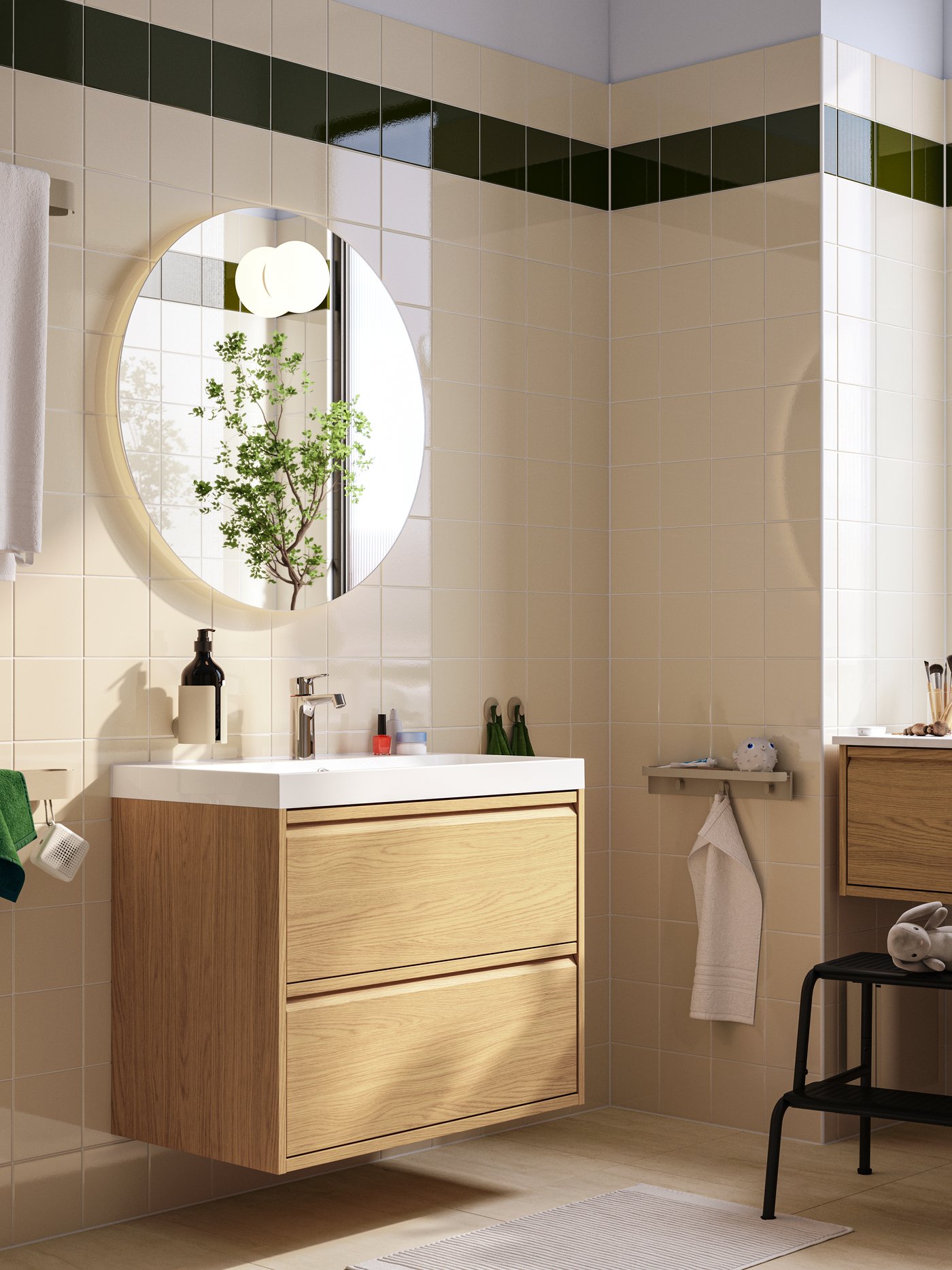 Un meuble lavabo ÄNGSJÖN/BACKSJÖN effet chêne avec deux tiroirs et un lavabo se trouve sous un miroir rond dans une salle de bains moderne.