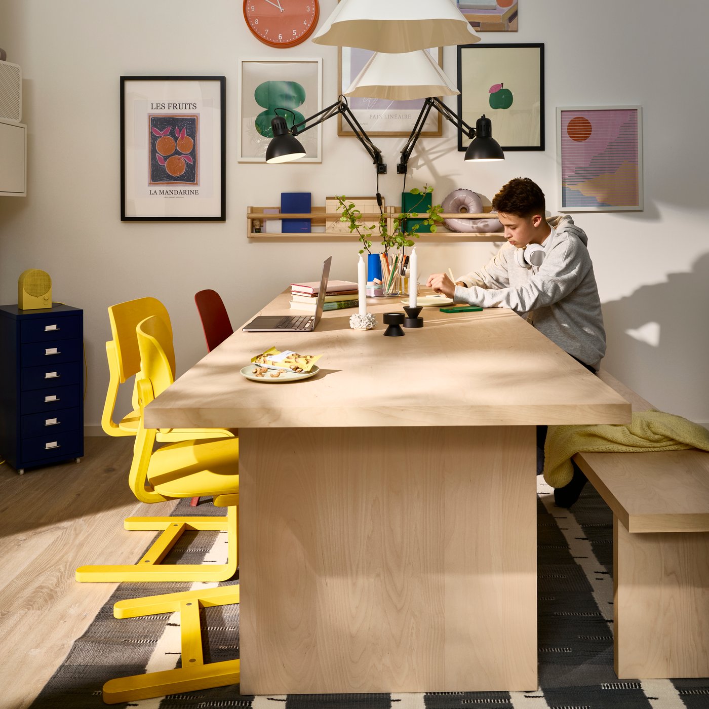 A person is sitting on a BERGSHYTTAN bench at a BERGSHYTTAN table that’s placed against a picture wall.