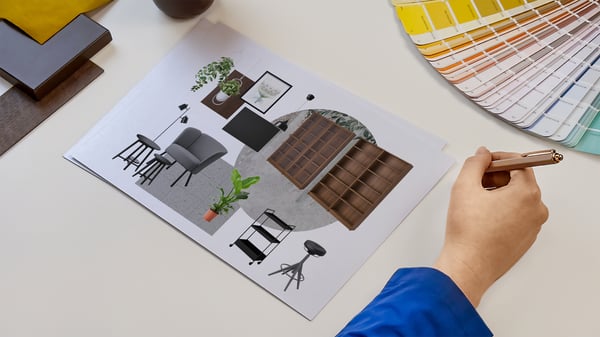 Projektantka wnętrz IKEA prezentująca kartki z wydrukiem kolażu produktowego zaprojektowanego pomieszczenia biznesowego. Obok na blacie leży wzornik kolorów i próbki materiałów.