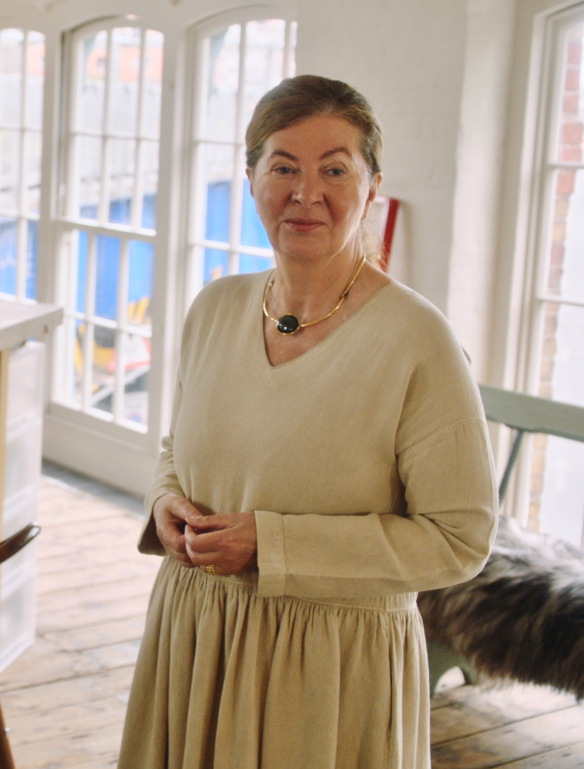 Ilse Crawford u beloj prostoriji, nosi bež haljinu i gleda u kameru.