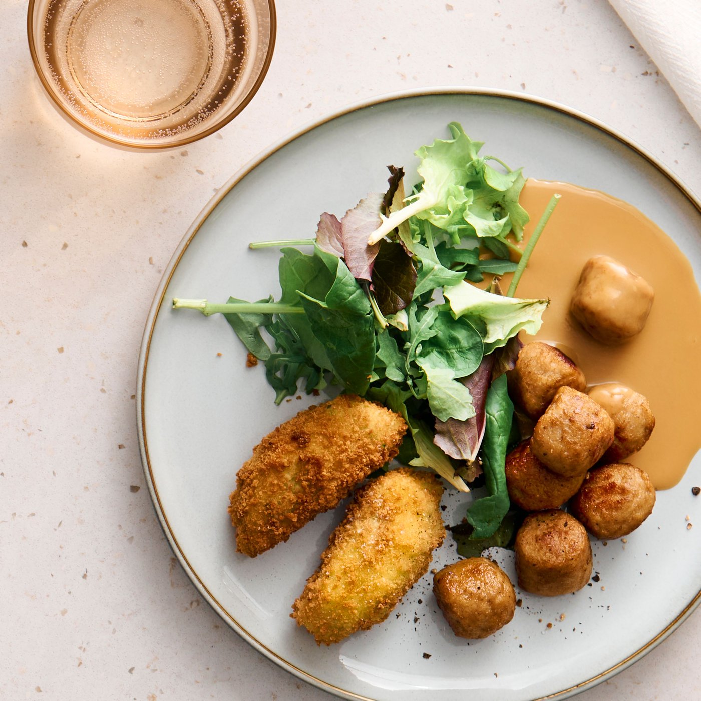 HUVUDROLL chicken meatballs served on a dinner plate with vegetable croquettes and mustard cream sauce.