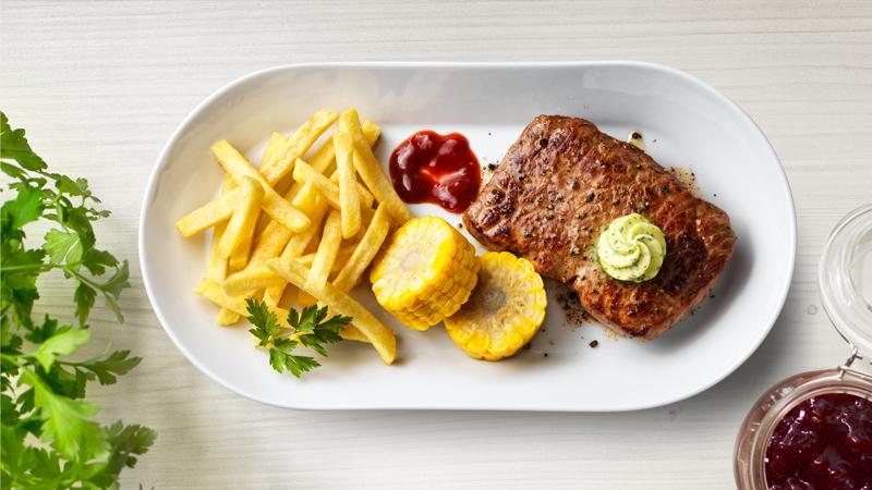 Ein weißer Teller mit einem Rumpsteak, Pommes und Maiskolben.