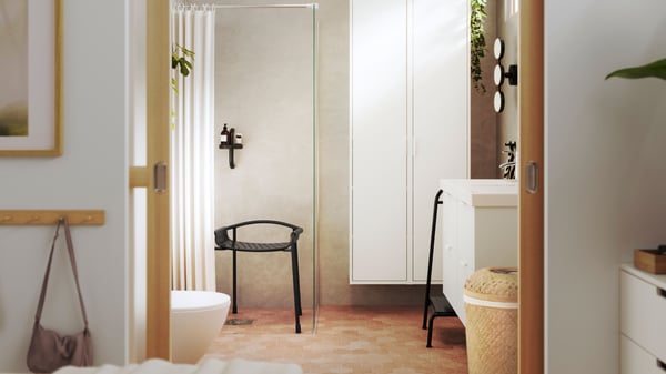 A bright bathroom is seen from a bedroom, and it has white HAVBÄCK bathroom furniture and BÄSINGEN accessories in anthracite.