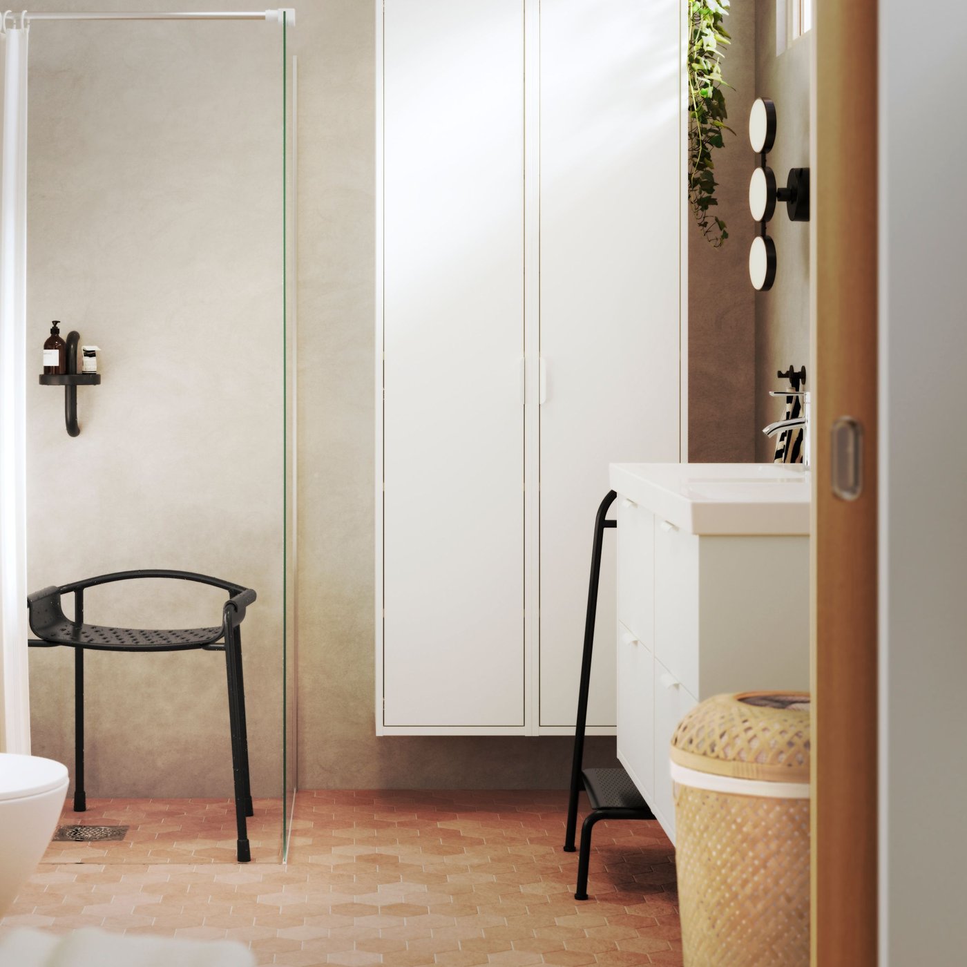 Pogled iz spalnice na svetlo kopalnico, opremljeno z belim HAVBÄCK kopalniškim pohištvom in antracitnimi BÄSINGEN dodatki.