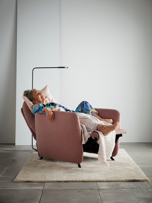 Living room with recliner in leaning position, high pile rug, floor lamp with LED, throw, person sitting in the recliner.
