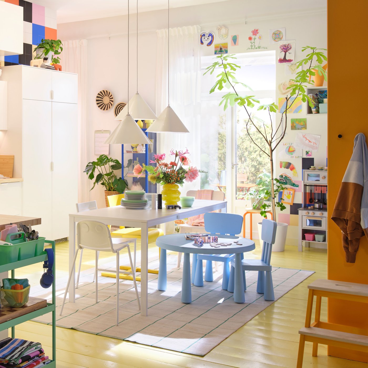 Es ist eine helle Küche mit weissen VEDDINGE Fronten, einem Holztisch und Topfpflanzen zu sehen.