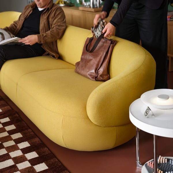 A person reaches into a bag that is laying against the backrest of  a LILLESÄTER 6-seat sofa in Gunnared bright green-yellow.