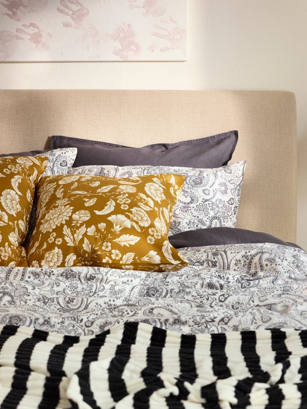 Close-up of bedding with RODGERSIA quilt cover and pillow cases, IDALINNEA cushion cover and striped blanket.