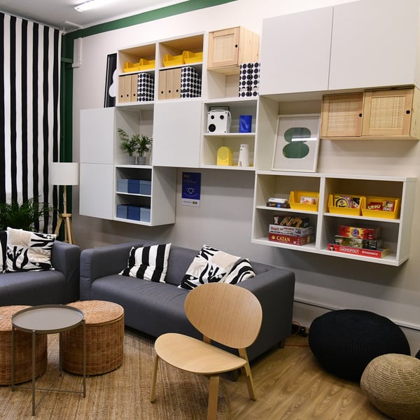 Wyposażona przestrzeń. Na ścianie białe wiszące szafki przed nimis zara sofa i brzozowe krzesła