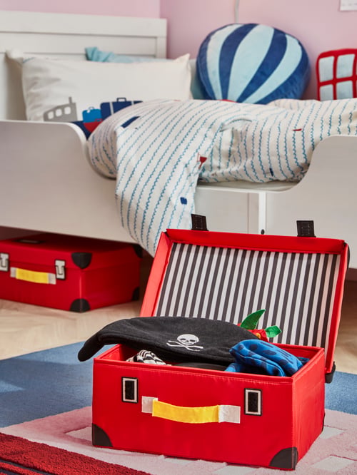 Kinderzimmer mit einem ausziehbaren SUNDVIK Bettgestell, gestreifter Bettwäsche, buntem Spielzeug und zwei FLYTTBAR Spielzeugkoffern, einer davon mit Kostümen gefüllt.