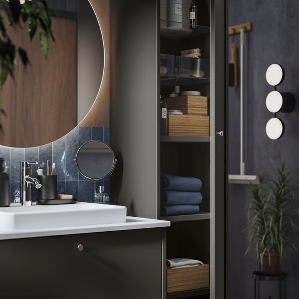 A modern, dark bathroom with a round FAXÄLVEN mirror and bathroom furniture, cabinets, and toiletries.