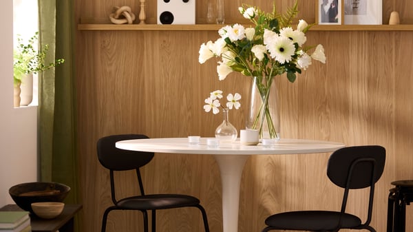 Two black SANDSBERG dining chairs stand by a white round table with a vase of white flowers in the dining room.