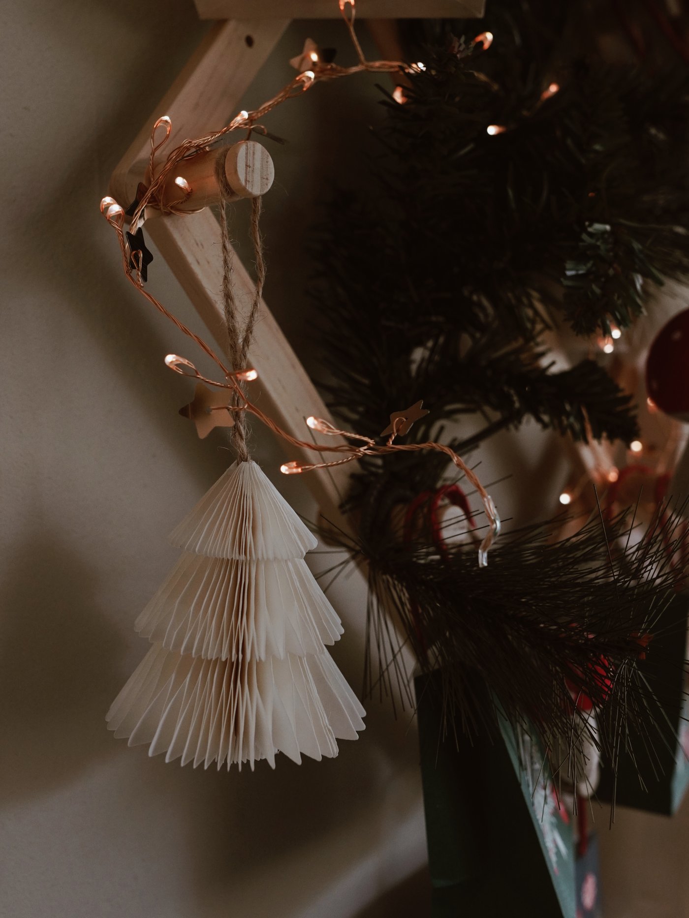 Une décoration de Noël en papier plié est accrochée à un mur orné de guirlandes lumineuses scintillantes. Avec son éclairage tamisé et ses nombreuses touches de verdure, la scène dégage une atmosphère chaleureuse et festive.