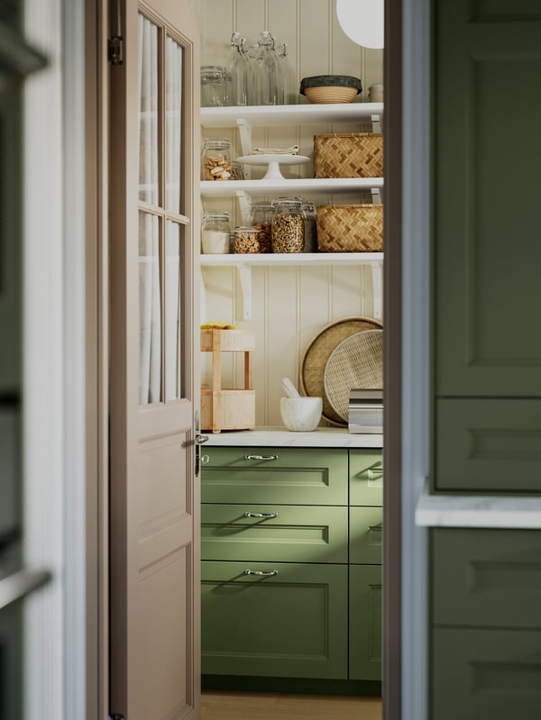 A store cupboard with AXSTAD grey-green kitchen fronts, open shelves with pots, baskets and kitchen utensils.
