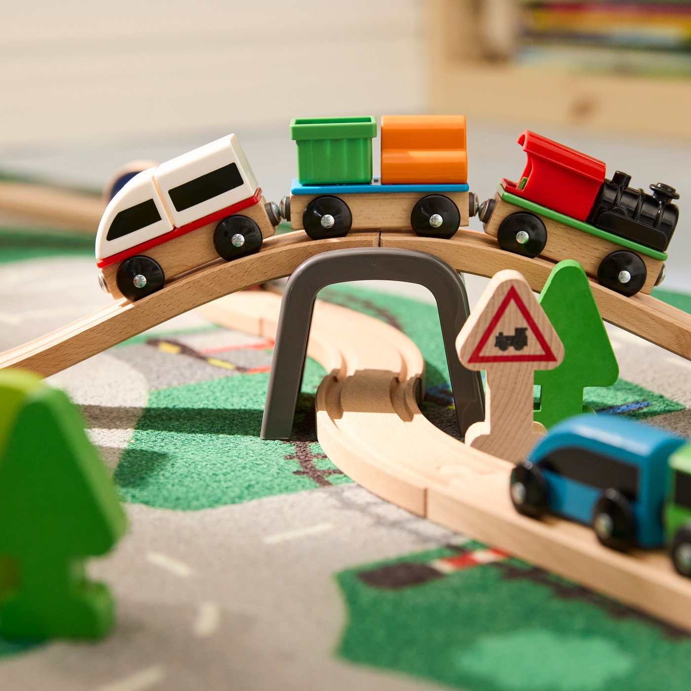 Primo piano di un set per trenino LILLABO con un trenino che passa sul ponte e un altro sul binario sottostante. I giocattoli si trovano su un tappeto LILLABO.