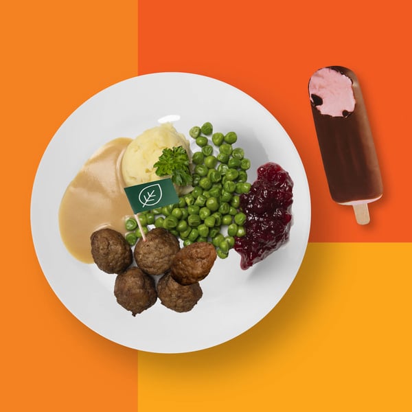 Lihaton pyörykkäannos perunamuusilla, herneillä ja puolukkahillolla oranssilla taustalla. Vieressä jäätelöpuikko.