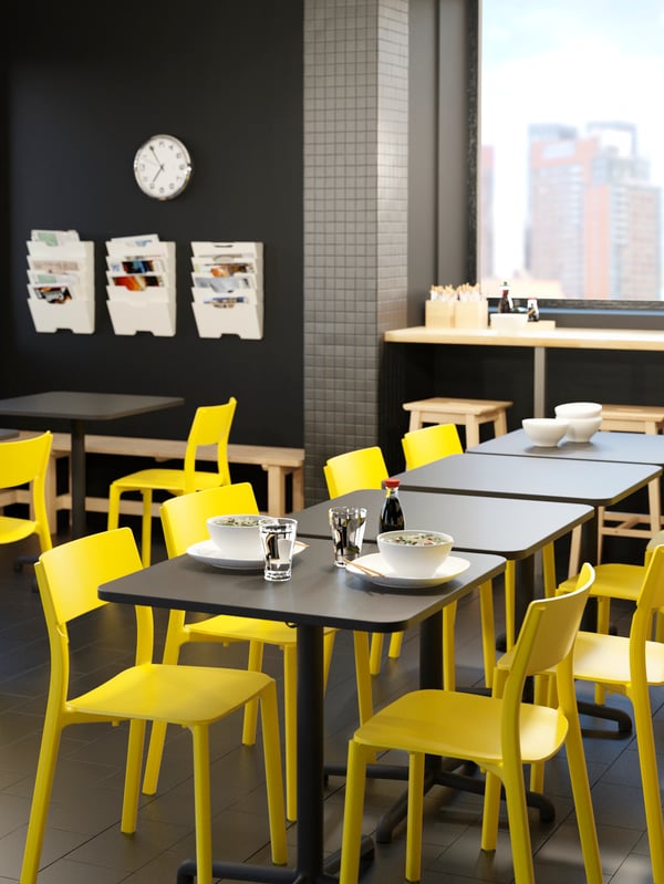 STENSELE tables with yellow JANINGE chairs put together in a lunchroom and set with two white plates and glasses.