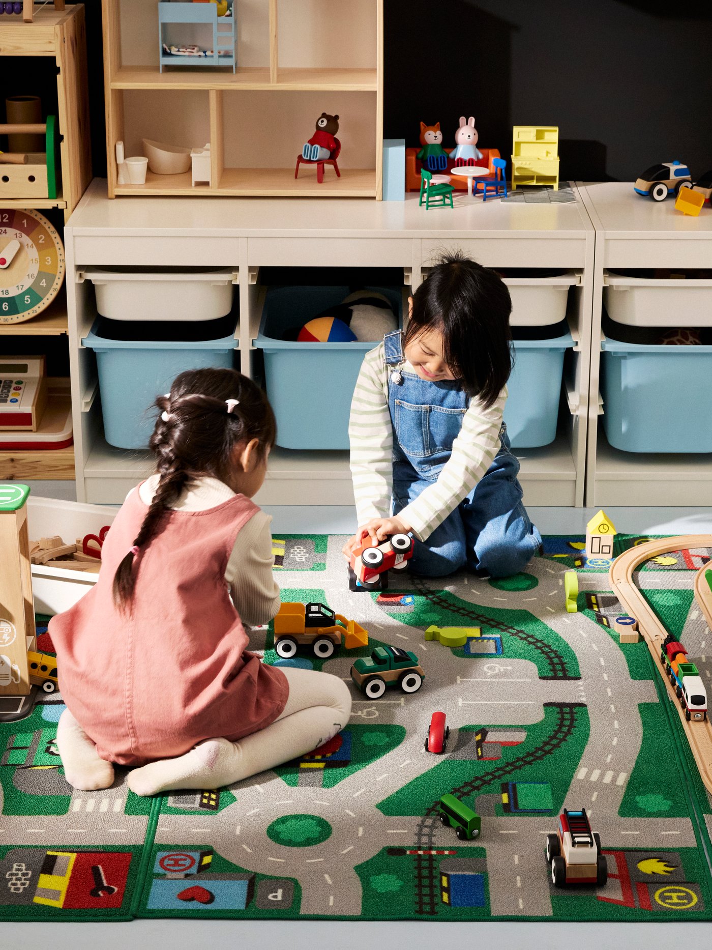 Two children playing with LILLABO toy vehicles, train set and garage, on the LILLABO rug. TROFAST storage boxes behind them.