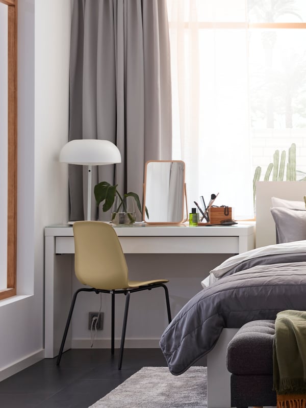 Una lámpara de trabajo TERTIAL de color gris oscuro junto a un sillón POÄNG de chapa de abedul/beige y una alfombra LOHALS de tejido plano en la esquina de una habitación.
