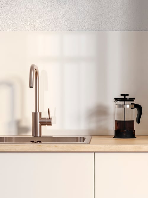 Un robinet de bucătărie și o chiuvetă cu inserție gri fixate pe un dulap de bază cu uși albe. Pe dulap este un filtru de cafea.