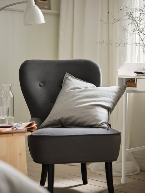 Living room with a grey armchair made of wood, with polyester cover, supporting a cushion cover next to a rectangular desk.