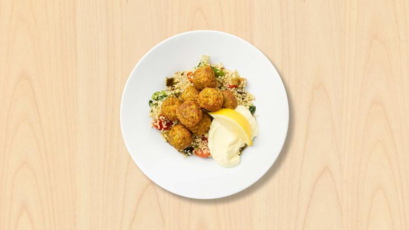Assiette blanche avec des falafels et du couscous au centre sur fond bois 