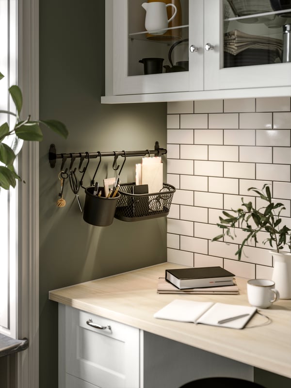 A corner in a kitchen with white ENKÖPING fronts has a nickel-plated HULTARP rail with hooks and containers above a worktop.