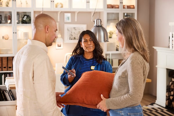 An IKEA interior designer helping two clients in a showroom, showing planning ideas on her smartphone.