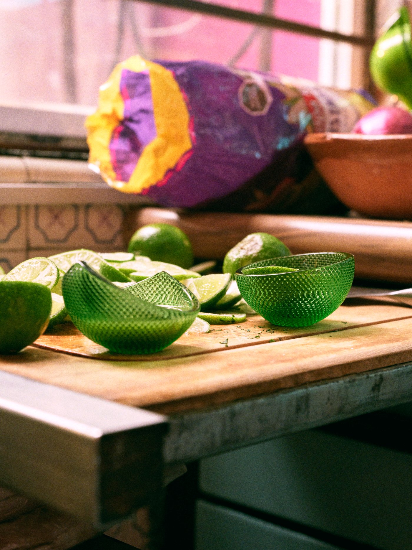 Dua mangkuk hidangan ÖMSESIDIG kaca berwarna hijau dengan corak timbul, limau nipis dan hirisan limau nipis pada permukaan kerja kayu.