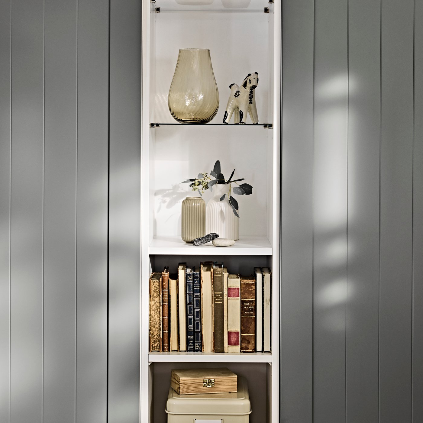 A section of the PAX/GULLABERG wardrobe combination displaying shelves with decor items and books in a bedroom.