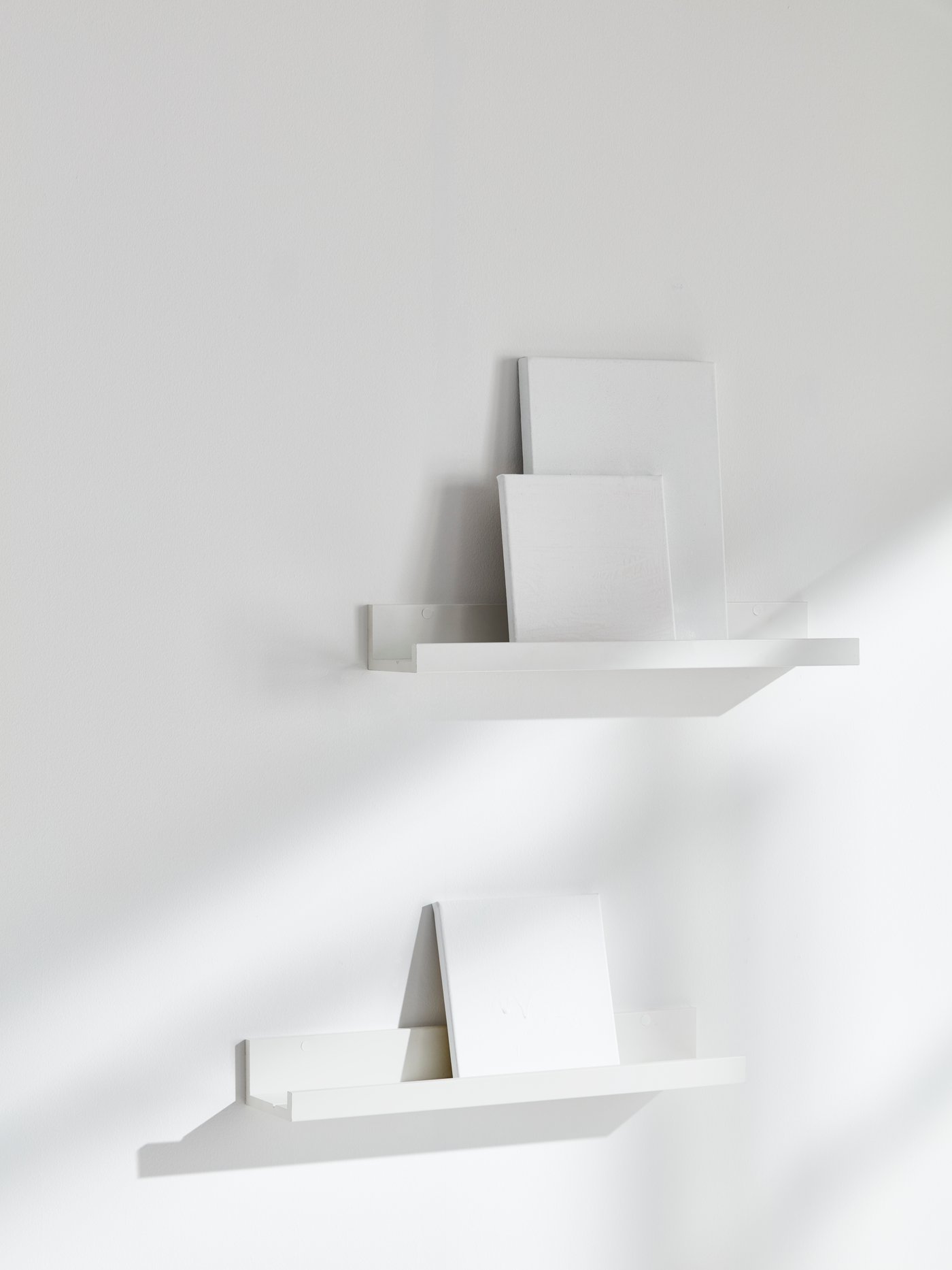 Two white MOSSLANDA picture edges sit against a white wall holding white books.