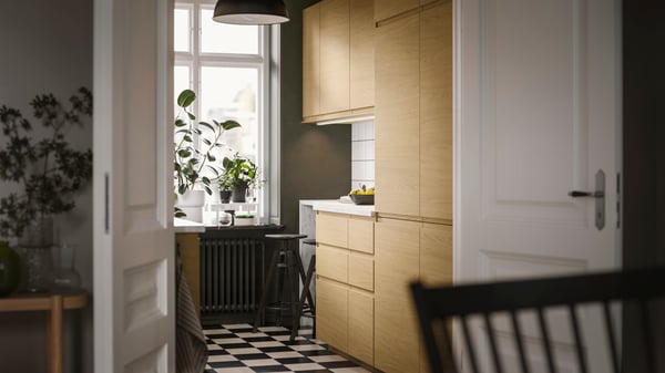 In una cucina, frontali VOXTORP effetto rovere con maniglie integrate e due sgabelli bar accanto al piano di lavoro.