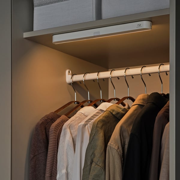 Beleuchtete Kleiderstange im Schrank mit ordentlich aufgehängten Hemden.