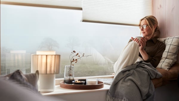 Una mujer sentada en el bow window con una tasa de té. En la venana hay cortinas eléctricas .