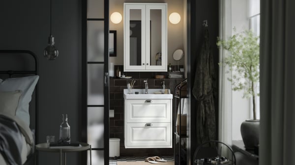 Een kleine, traditionele badkamer met wit TÄNNFORSEN opbergmeubels, twee ronde lampen en zwarte details.