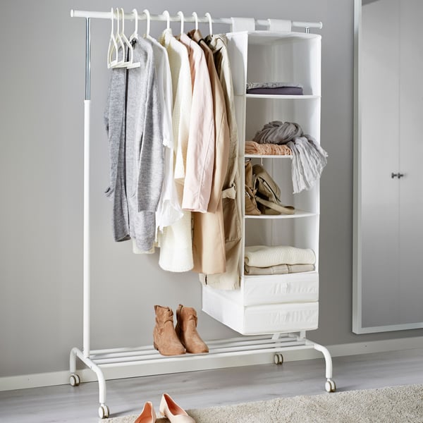 A MULIG clothes rack in the middle of a bedroom with clothes hanging on it.