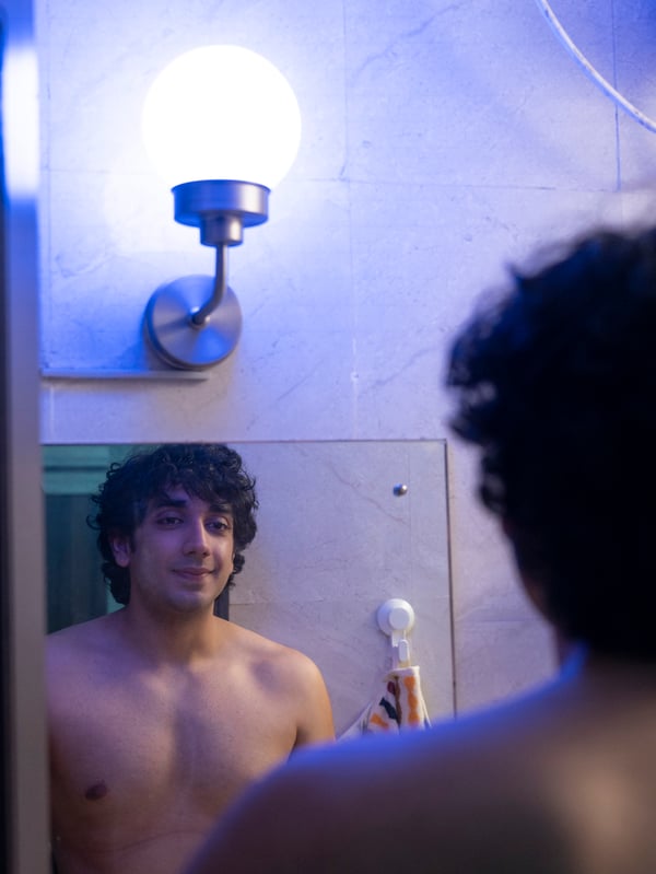A man looks himself in the bathroom mirror. The lighting is blue.