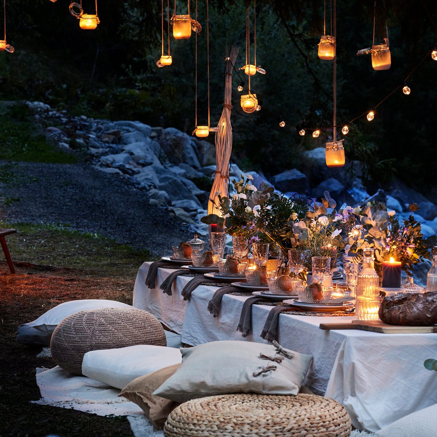 En kvällsbild på ett festligt dukat långbord utomhus med massor av ljus, lyktor och slingor.