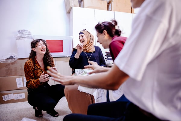 Vier Frauen lachen und erzählen sich Geschichten in einer gemütlichen, lockeren Atmosphäre, umgeben von Kartons. Die gute Laune und der Zusammenhalt sind echt spürbar.