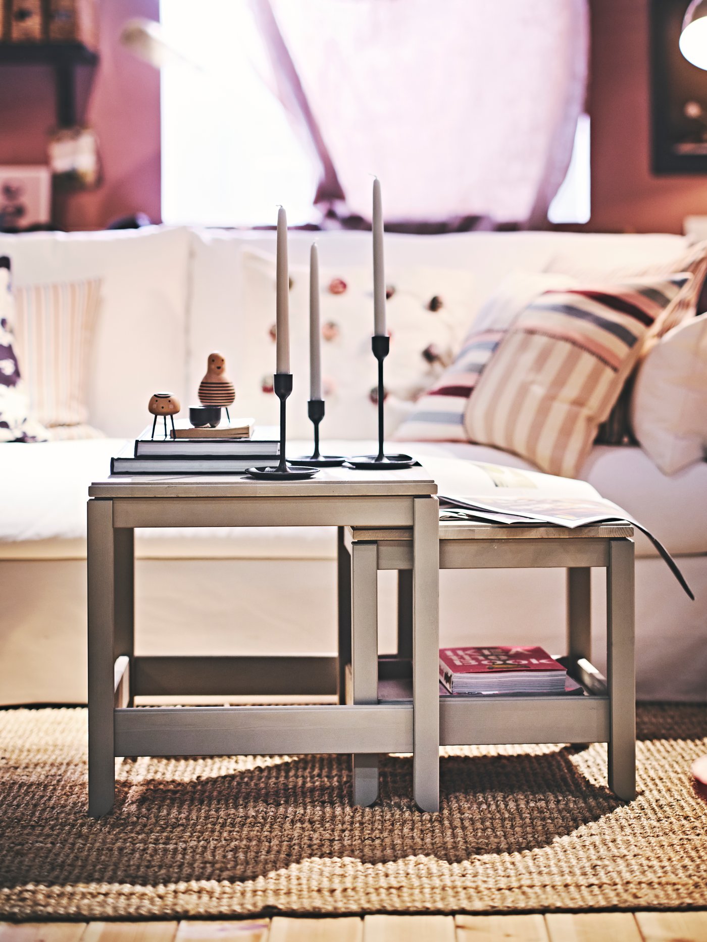 Gemütliches Wohnzimmer mit weißem Sofa, dekorierten Kissen, Holz-Couchtisch mit Kerzenhaltern und Teppich.