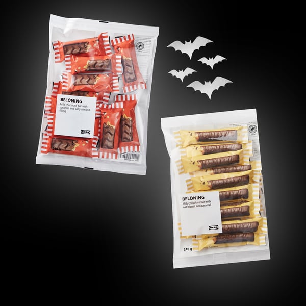 Deux tablettes de chocolat au lait BELÖNING sont placées sur un fond noir, avec des chauves-souris blanches découpées à droite.