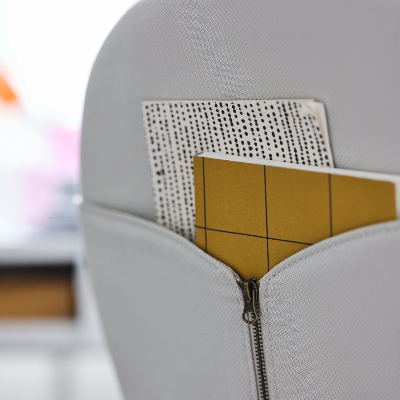 Respaldo de la silla giratoria BJÖRKBERGET beige con 2 cuadernos en el bolsillo con cierre formado por las solapas de tela.