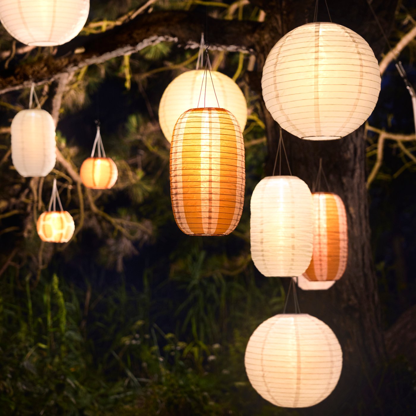 An outdoor area is illuminated by many white and striped orange SOLVINDEN pendant lamps that enhances the ambiance.
