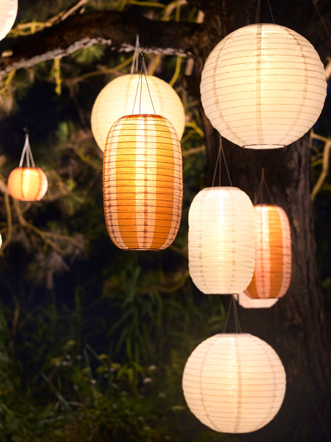 An outdoor area is illuminated by many white and striped orange SOLVINDEN pendant lamps that enhances the ambiance.