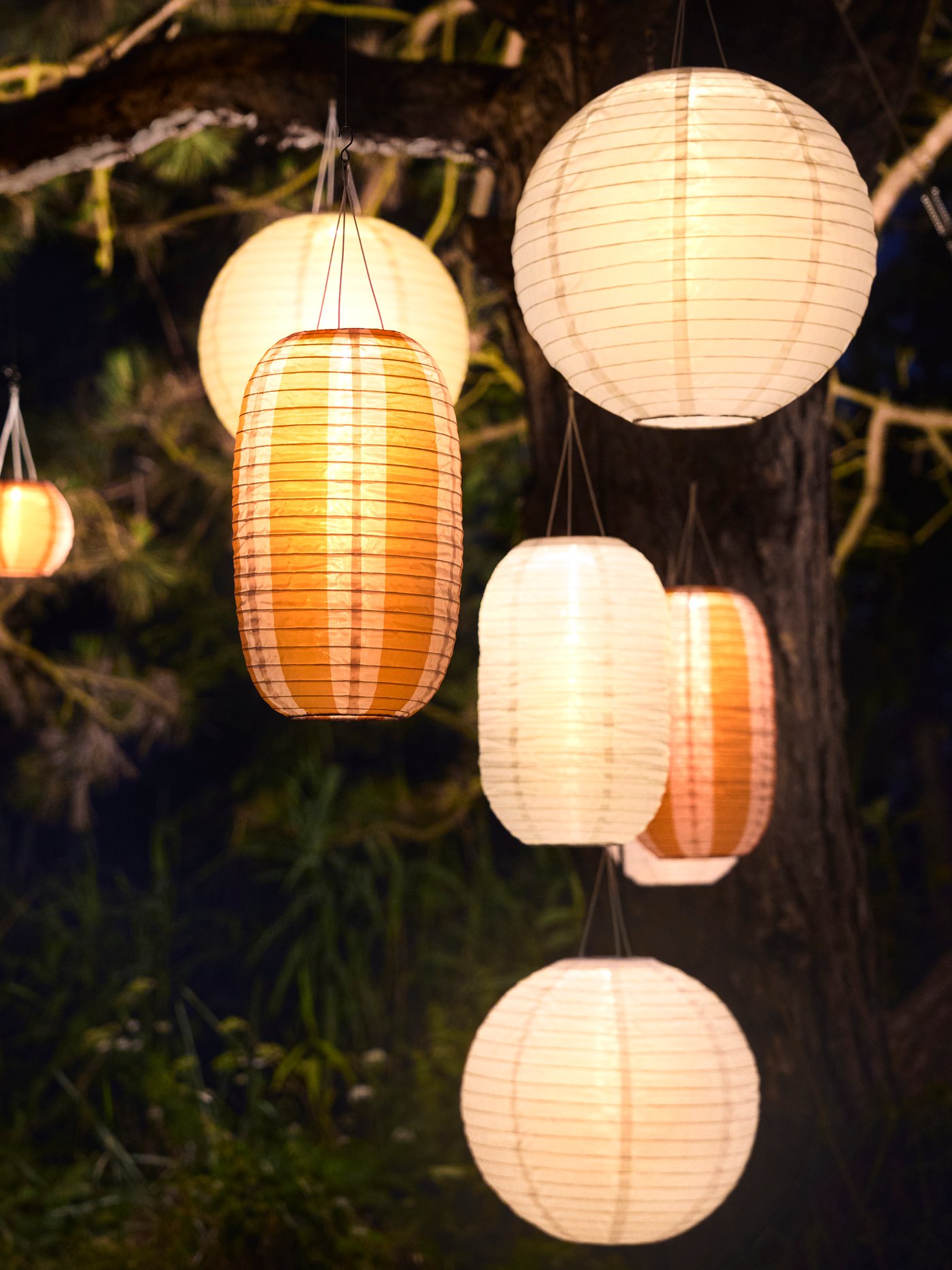 Een buitenruimte die wordt verlicht door meerdere witte en oranje‑gestreepte SOLVINDEN hanglampen, waardoor de sfeer extra wordt versterkt.