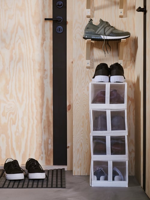 A modern hallway that features a rectangular shoe box holding several pairs of shoes next other to pairs of shoes.