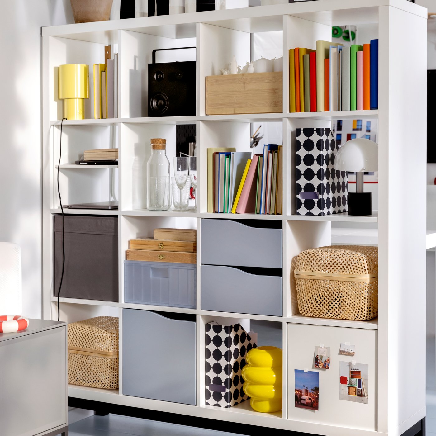 Een witte KALLAX kast met veel objecten op de planken, inclusief KALLAX inzetstukken, staat op een zwart KALLAX onderstel.